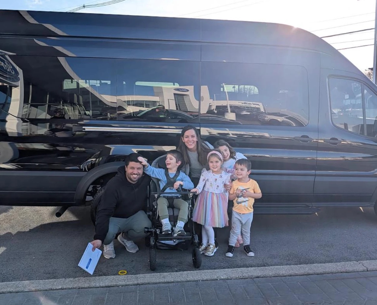 A family celebrates picking up their new wheelchair accessible van, one child in a power wheelchair
